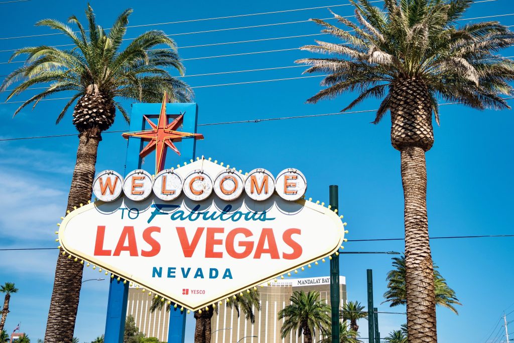 A sunny day view of the iconic 'Welcome to Fabulous Las Vegas' sign surrounded by palm trees, with a clear blue sky overhead.